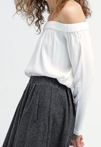 Blusa blanca sin mangas con escote fruncido, combinada con una falda plisada gris oscuro que presenta bolsillos laterales y una tela texturizada.
