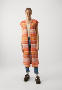 Long gilet ouvert à l'avant présentant un motif en zigzag multicolore dans des tons d'orange, de rose et de blanc, avec des manches courtes et une texture légère.