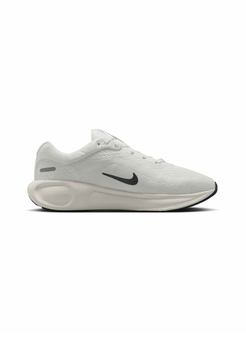 Zapatilla deportiva de color gris claro con parte superior de malla texturizada, swoosh negro de Nike, diseño de cordones y una suela de goma negra en contraste.