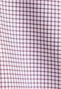 Tissu blanc avec un motif en grille de petits carreaux bruns, texture tissée visible, carrés espacés de manière égale formant un dessin répétitif.