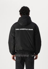 Black puffer jacket with a hood, featuring white "KARL LAGERFELD JEANS" branding on the back, and elasticated hem and cuffs.