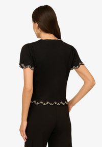 Černý krátký rukáv top s vlnitým lemem, zdobený kulatými ozdobami kolem výstřihu a rukávů, s přiléhavým střihem.