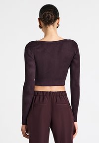 Top corto a maniche lunghe a coste di un viola scuro con scollatura ampia, abbinato a pantaloni a vita alta coordinati con un elastico in vita.