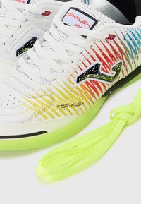 Baskets blanches de sport avec un design dégradé présentant des rayures rouges, jaunes et bleues. Un logo noir et des lacets néon verts vifs inclus.