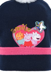 Berretto di maglia blu navy con una fascia rosa. Presenta una toppa a forma di cuore con personaggi colorati e ricamo "smile", sormontato da un pom-pom bianco.