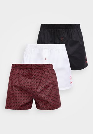 Drei Paar elastische Herrenboxershorts in Schwarz, Weiß und Rot mit Herzmustern, übereinander liegend auf hellem Hintergrund angeordnet.
