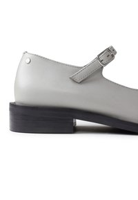 Grauer Lederschuh mit einem niedrigen schwarzen Blockabsatz, verstellbarem Knöchelriemen und minimalen Nähdetails. Schlankes Design mit geschlossener Zehenpartie.