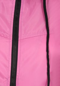 Felle roze stof met een gladde textuur, voorzien van een zwarte ritssluiting in het midden en contrasterende zwarte stiksels langs de randen.