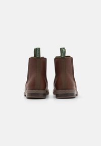 Bottes Chelsea en cuir marron avec des panneaux élastiques sur les côtés, des poignées vertes et un talon empilé. Surface texturée et détails de couture contrastants.