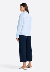 Camisa a rayas azul claro y blanca con un cuello con volantes, combinada con pantalones de pierna ancha en azul marino y mules de tacón bajo color crema.