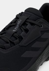 Schwarzer Sportschuh mit atmungsaktivem Mesh-Obermaterial, Gummisohle und verstärkten Akzenten; auf der Zunge befindet sich das "TERREX"-Logo.