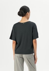 Black short-sleeve t-shirt with a relaxed fit, featuring a subtle golden accent at the neckline. Paired with light gray wide-leg trousers.