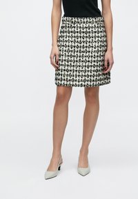 Sort-hvid ternet tweednederdel med lige snit, knælængde og subtil tekstur. Kombineret med lyse sko med hæl.