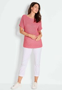 Roze gebreide top met een losse fit en korte mouwen, gecombineerd met opgerolde witte broeken en witte sneakers. Soepele textuur, horizontale strepen.