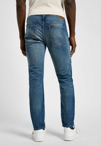 Wąskie niebieskie dżinsy z efektem sprania, z dwiema tylnymi kieszeniami i akcentami w postaci szwów. Połączone z białymi trampkami.