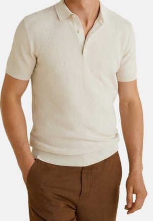 Beige kortærmet polo med et tekstureret mønster, der har en krave og en tredobbelt knapstolpe, kombineret med brune bukser.