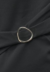 Tecido negro drapeado com um anel prateado de forma irregular, exibindo uma textura suave e um brilho sutil.