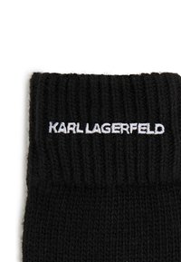 Meia preta tricotada com textura canelada. Apresenta o logótipo branco bordado "KARL LAGERFELD" na parte superior. Material suave e ajuste confortável.