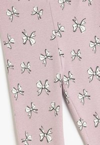 Ljusrosa strukturerad tyg med ett upprepande mönster av svarta och vita rosetter, vilket skapar en lekfull och detaljerad design.