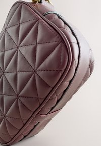 Quiltet håndtaske i burgunderrødt læder med geometrisk mønster, rund form, guldfarvet hardware og kontrastkanter.
