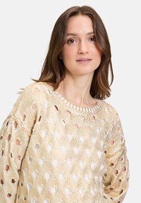 Strickpullover in goldbeige mit offenem Rautenmuster. Runder Ausschnitt, lange Ärmel und strukturierte Oberfläche verleihen ihm ein leichtes, luftiges Aussehen.