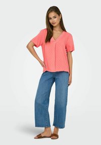 Roze textuur blouse met een V-hals en korte mouwen, gecombineerd met lichtblauwe wijde jeans en bruine slippers.