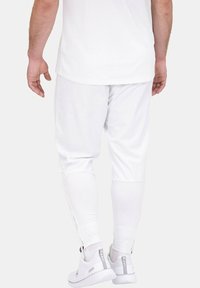 Weiße Jogginghose mit schmalem Schnitt, Reißverschluss an den Knöcheln und glatter Textur, kombiniert mit weißen Sneakers.