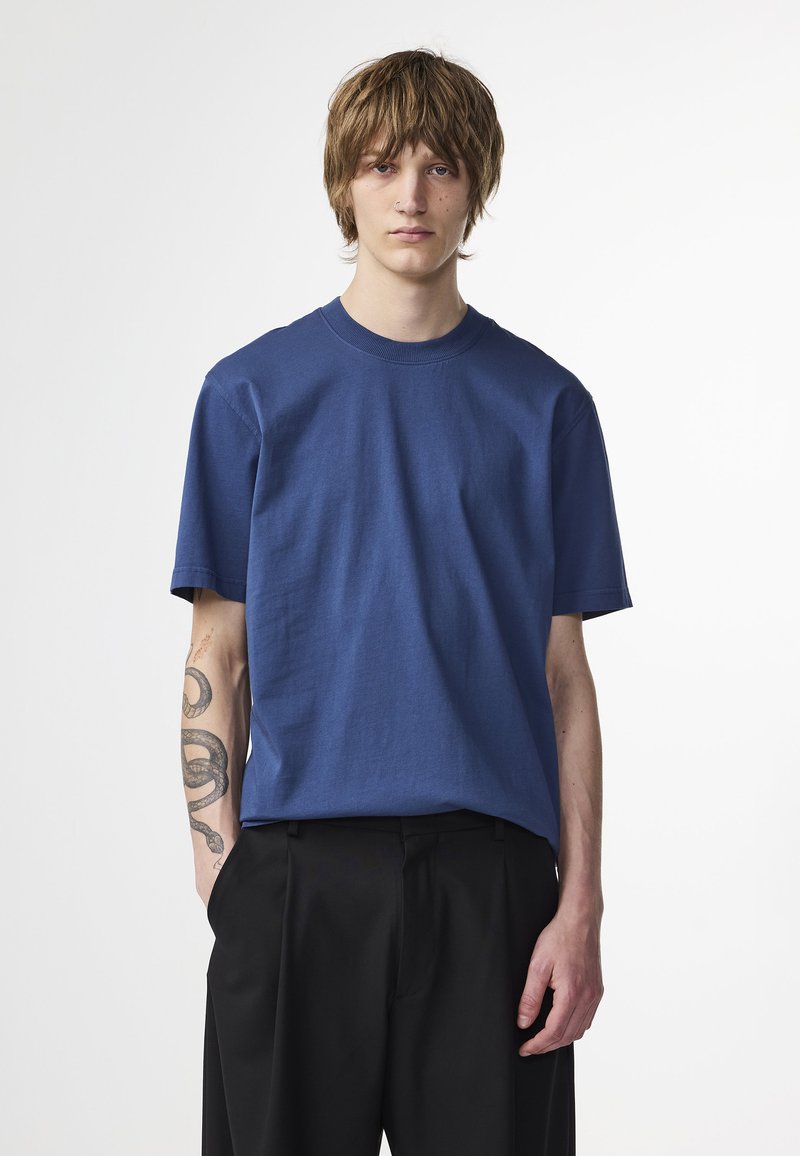 Kortsleeve blå bomulls t-shirt med rund halsringning, slät textur och avslappnad passform, kombinerad med svarta byxor. Inga anmärkningsvärda mönster.