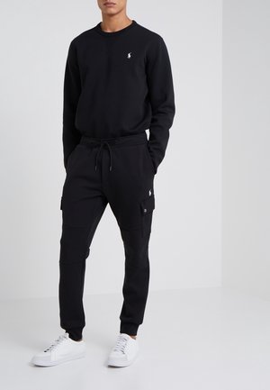 Czarna bluza z kapturem i spodnie cargo wykonane z miękkiego materiału, z małym logo na piersi i kieszeniami po bokach, zestawione z białymi trampkami.