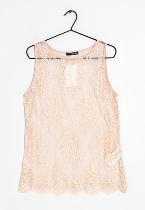 Blouse sans manches en dentelle transparente couleur pêche clair avec motifs floraux, encolure ronde et ourlet festonné, suspendue sur un cintre noir.