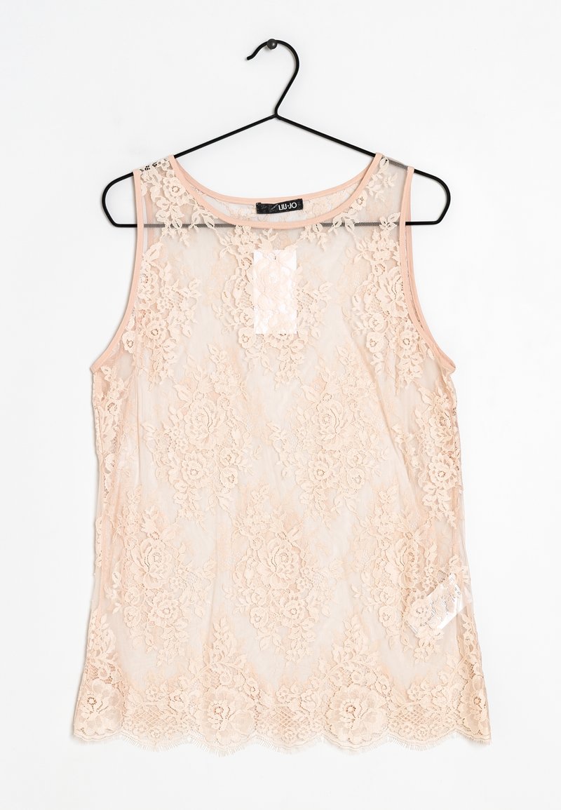 Blouse sans manches en dentelle transparente couleur pêche clair avec motifs floraux, encolure ronde et ourlet festonné, suspendue sur un cintre noir.