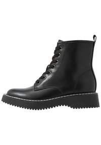 Zwarte leren veterschoen tot de enkel met een ronde neus, dikke zool en witte stiksels langs de rand. Heeft een trekhaak bij de hiel.