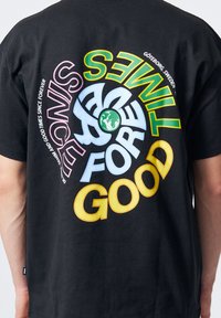 Camiseta de algodón negra con gráficos de texto audaces y coloridos: "DESDE SIEMPRE" en rosa, verde, azul y amarillo alrededor de un símbolo de globo.