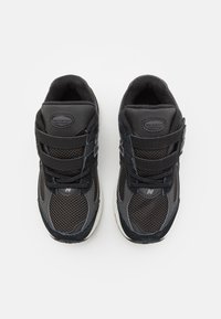 Baskets de sport noires avec une tige en maille et en daim, deux bandes velcro, des panneaux texturés et une semelle en caoutchouc blanche.