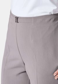 Helle graue Hose mit einer glatten, strukturierten Oberfläche, einem Bund und einem Frontverschluss, die eine taillierte Passform und klare Linien präsentiert.