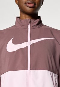 Ζακέτα Nike με φερμουάρ, που διαθέτει ψηλό γιακά, σχεδιασμό με μπλοκ χρωμάτων σε μωβ και ανοιχτό ροζ, με το χαρακτηριστικό λευκό λογότυπο Swoosh στο στήθος.
