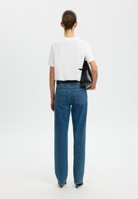 Witte, shirts met korte mouwen gecombineerd met hoge, blauwe spijkerbroeken. Zwarte handtas in één hand. Rechtaflopende pasvorm, minimale details.