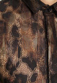 Blusa negra transparente con un patrón de leopardo y acentos dorados, textura estructurada y un cuello con cierre de botones.