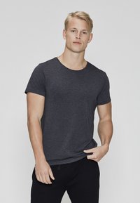 Mørkegrå t-shirt i blødt, let stof; rund halsudskæring; korte ærmer; tætsiddende design; båret med sorte bukser; glat tekstur.