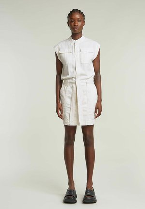 Robe blanche sans manches avec deux poches avant, taille ceinturée et coupe droite. Associée à des chaussures noires à enfiler. Texture lisse.