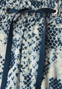 Navy drawstring on a light blue fabric with a snake skin pattern; features a metal eyelet and textured surface.