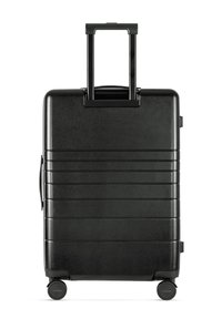 Black hard-shell suitcase with a textured surface, horizontal grooves, retractable handle, and four swivel wheels for easy mobility.