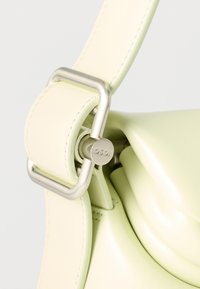 Κοντινό πλάνο του λουριού τσάντας από ανοιχτό πράσινο δέρμα με ασημένια τετράγωνη αγκράφα και κυλινδρικό κούμπωμα χαραγμένο με "OSOI".