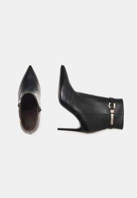 Black leather ankle boots with pointed toes and high stiletto heels, featuring a side zipper and a decorative strap with a metal buckle.