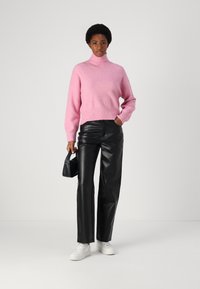 Hellrosa Rollkragenpullover, oversized Passform, weicher Stoff; kombiniert mit hoch taillierten schwarzen Lederhosen; accessorized mit einer kleinen schwarzen Tasche.