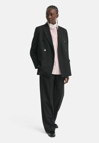 Black double-breasted blazer with large buttons, worn over a white and red striped shirt and wide-leg black trousers. Smooth fabric, tailored fit.