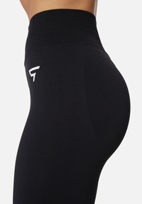 Black leggings made from stretchy fabric, featuring a high waistband and a small white logo on the thigh, emphasizing a fitted shape.