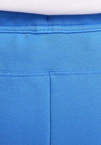 Närbild av blått tyg med detaljerad sömnad vid en söm mot en vit bakgrund.