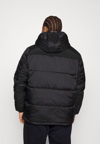 Giubbotto imbottito nero con cappuccio. Presenta un design a righe orizzontali, una texture lucida e pannelli neri a contrasto sulle spalle.