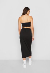 Crop top noir côtelé et jupe longue, tous deux dotés d'un design ajusté et d'un tissu extensible. Portés avec des baskets blanches et des chaussettes de cheville.